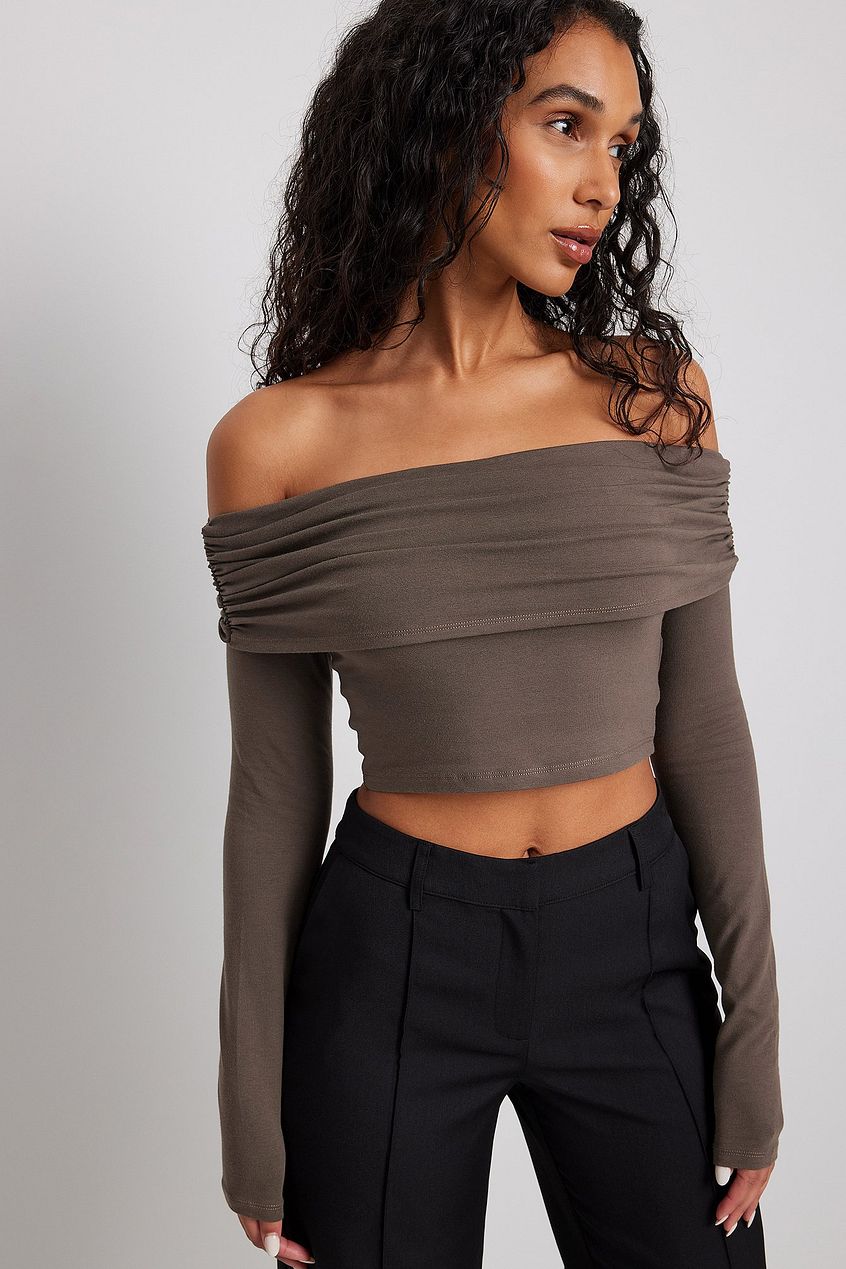NA-KD brown off-shoulder long sleeve top. This top is cropped and features an off shoulder look with long sleeves and comes in brown.