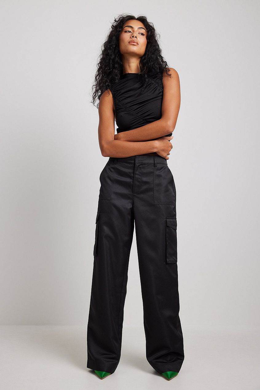 NA-KD black satin cargo pants with a high waist and two front cargo pockets. They have two back pockets with flaps and two side pockets. These cargo pants feature satin fabric.